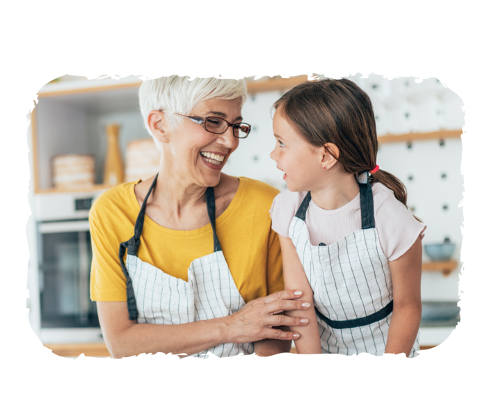 Leben mit CML Eine Frau und ein junges Mädchen tragen Kochschürzen und lachen. Vor ihnen liegen verschiedene Lebensmittel auf einem Tisch.
